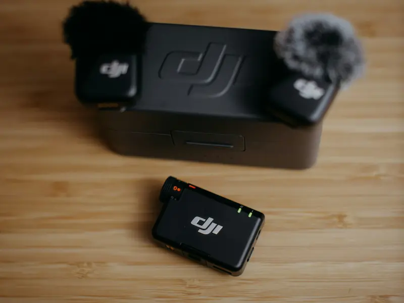 Deux micros sans fil DJI avec bonnettes anti-vent posés sur leur boîtier de charge, et le récepteur devant