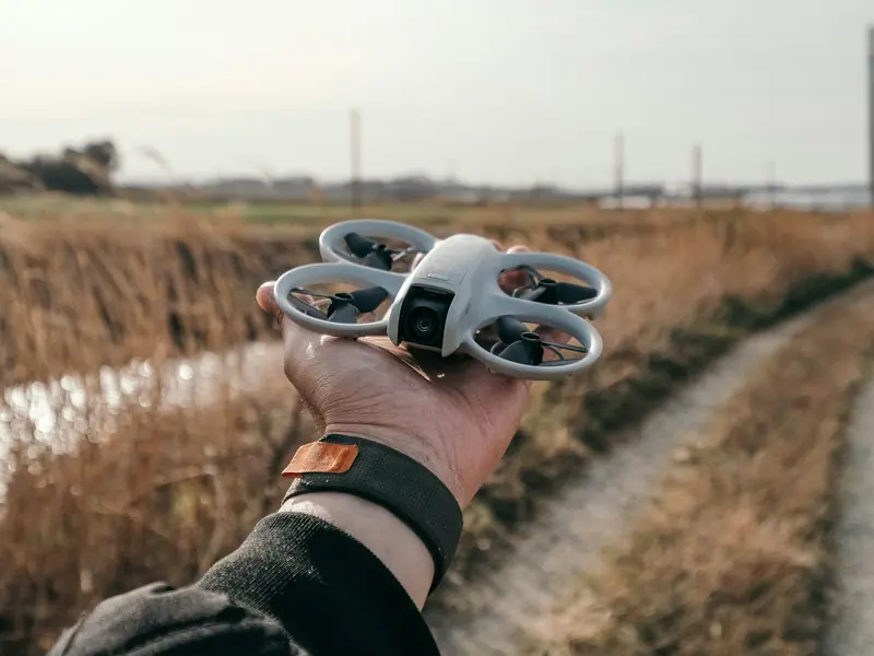 Un mini drone DJI Neo blanc à hélices protégées, posé dans la paume d'une main au bord d'un chemin